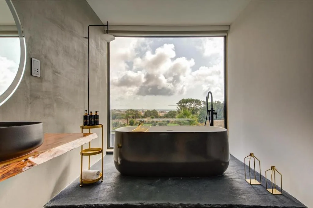 A freestanding black bath in front of a window over the fields
