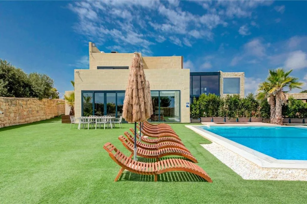 The pool, loungers and the house behind under a full sun